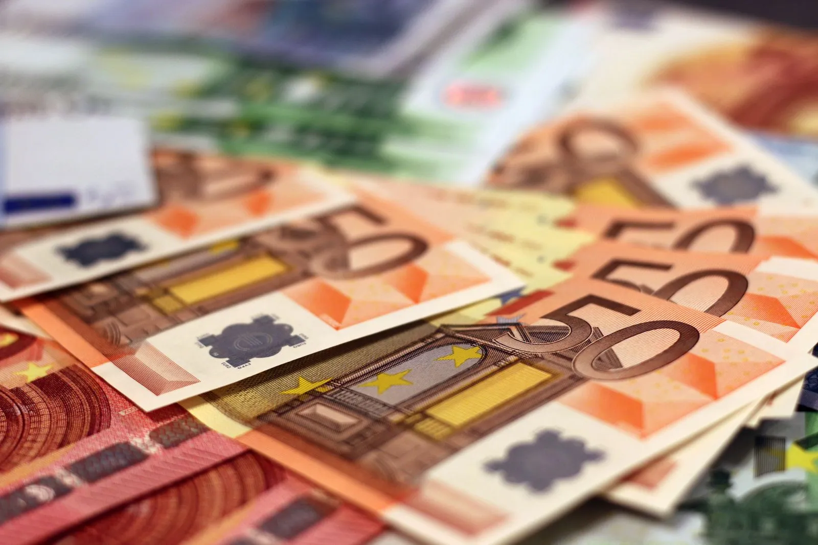 Primo piano di banconote in euro disposte a ventaglio, soprattutto biglietti arancioni da €50, con banconote da €10 e €100 intorno
