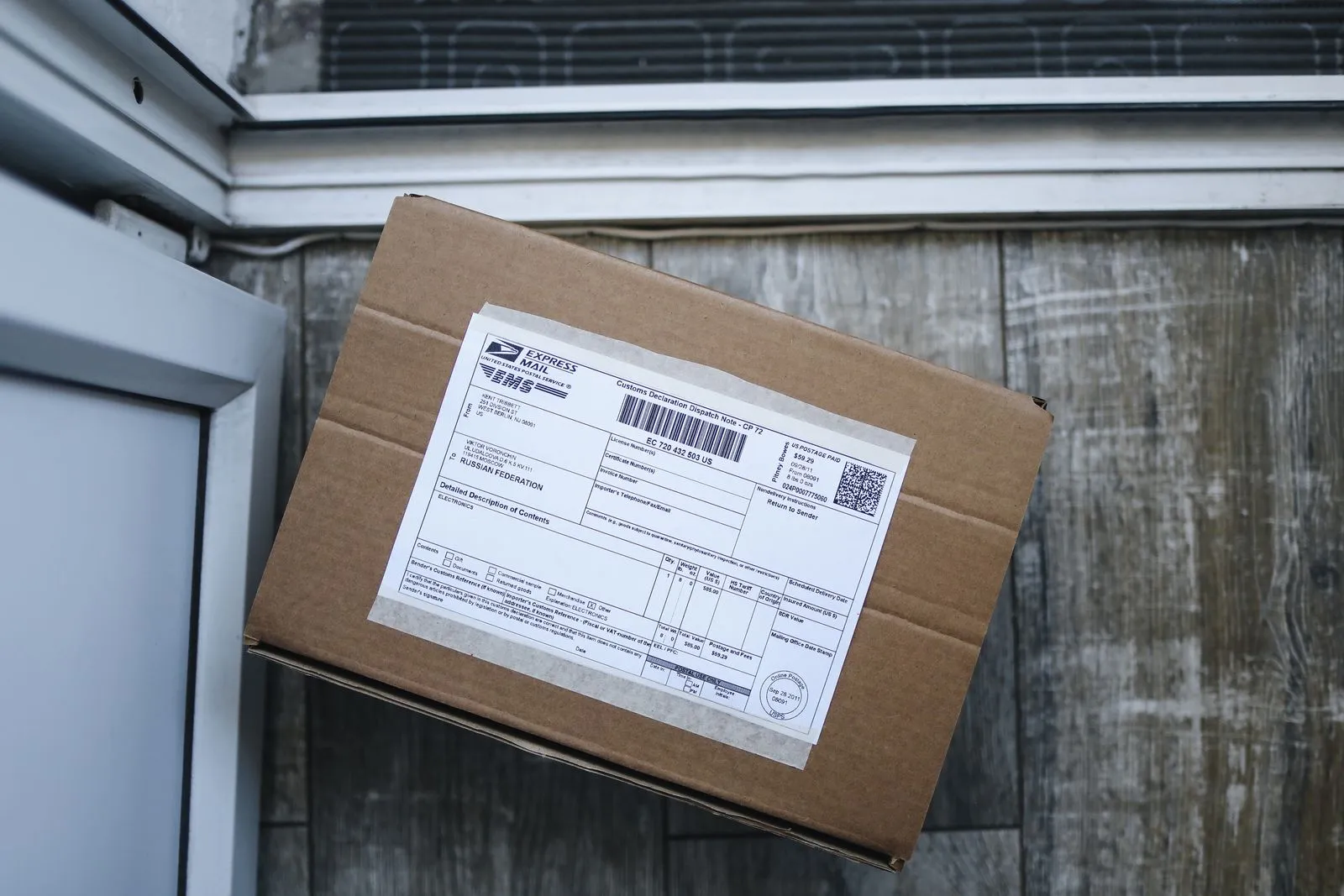 Un pacco di cartone con la dichiarazione doganale postale applicata sul coperchio, appoggiato a una parete di legno consumata