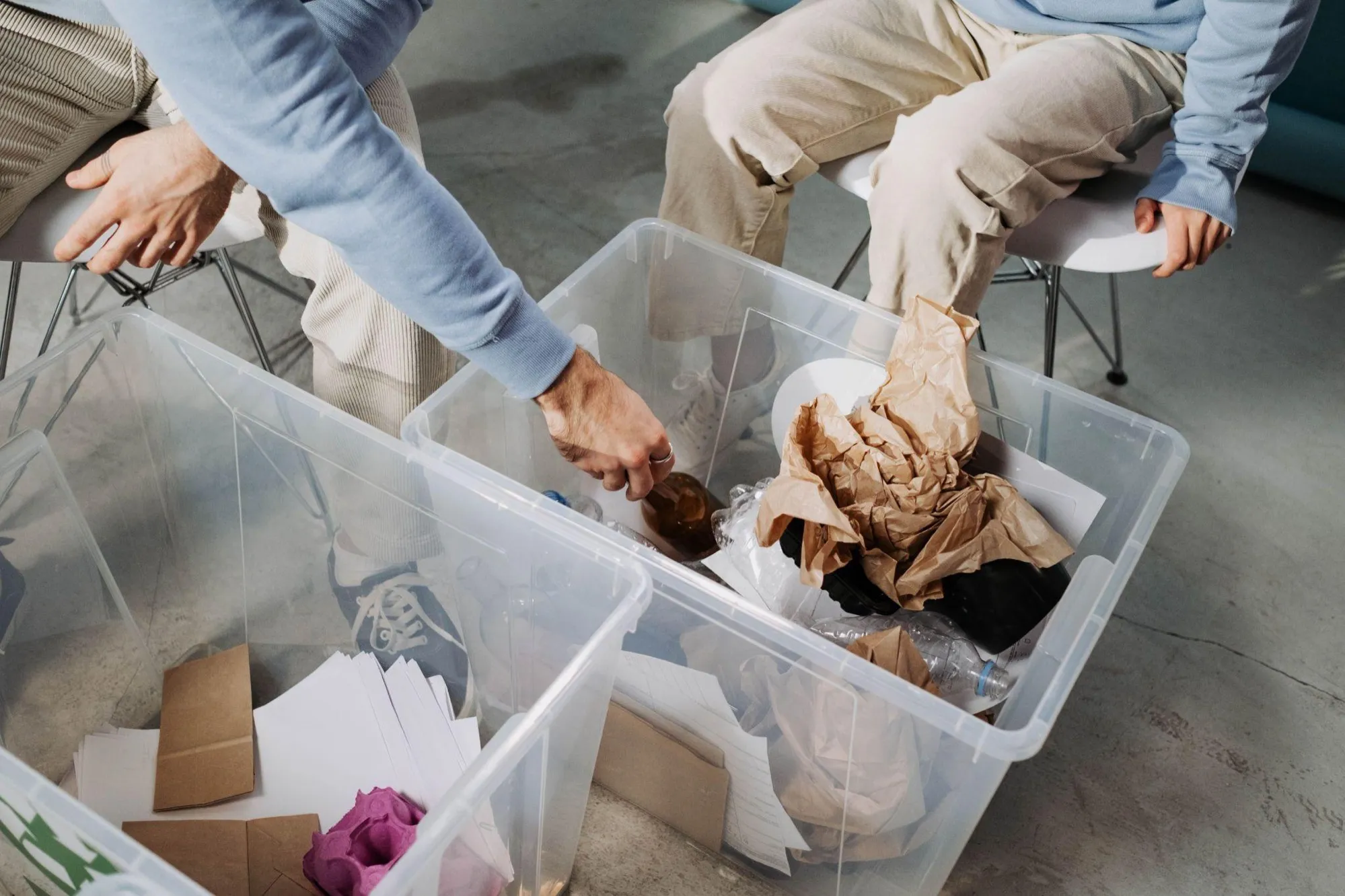 Due persone separano rifiuti da imballaggio — carta, film plastico e cartone — in contenitori trasparenti