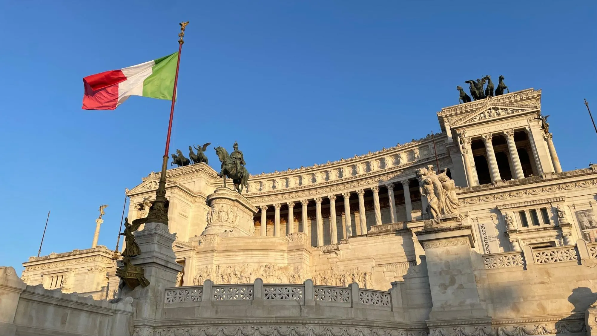 The Italian flag flying beside the Vittoriano monument in Rome against a clear blue sky
