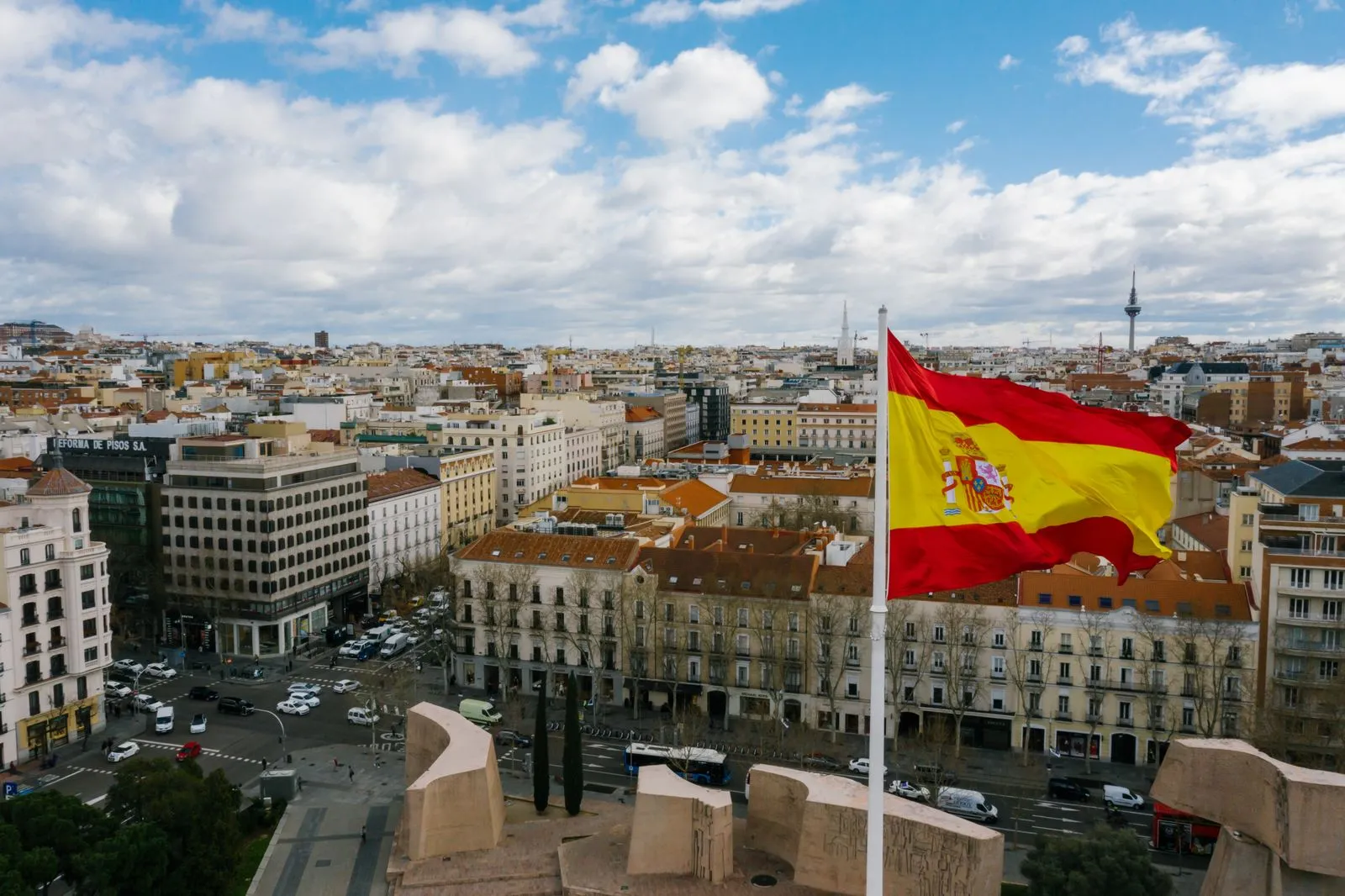 曇り空の下、マドリードの街並みの上ではためくスペイン国旗