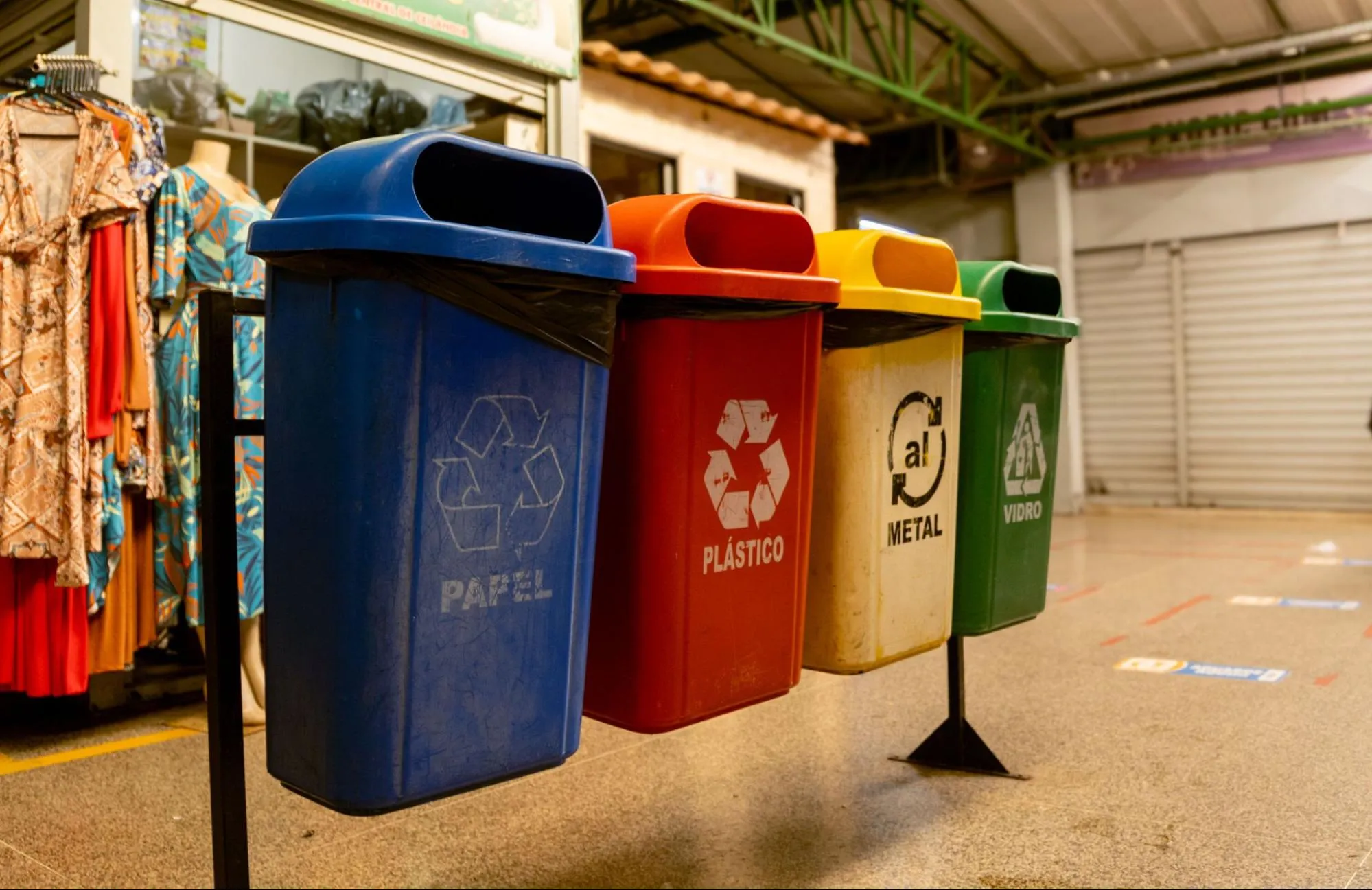 Four coloured recycling bins for paper, plastic, metal and glass lined up in a market hall
