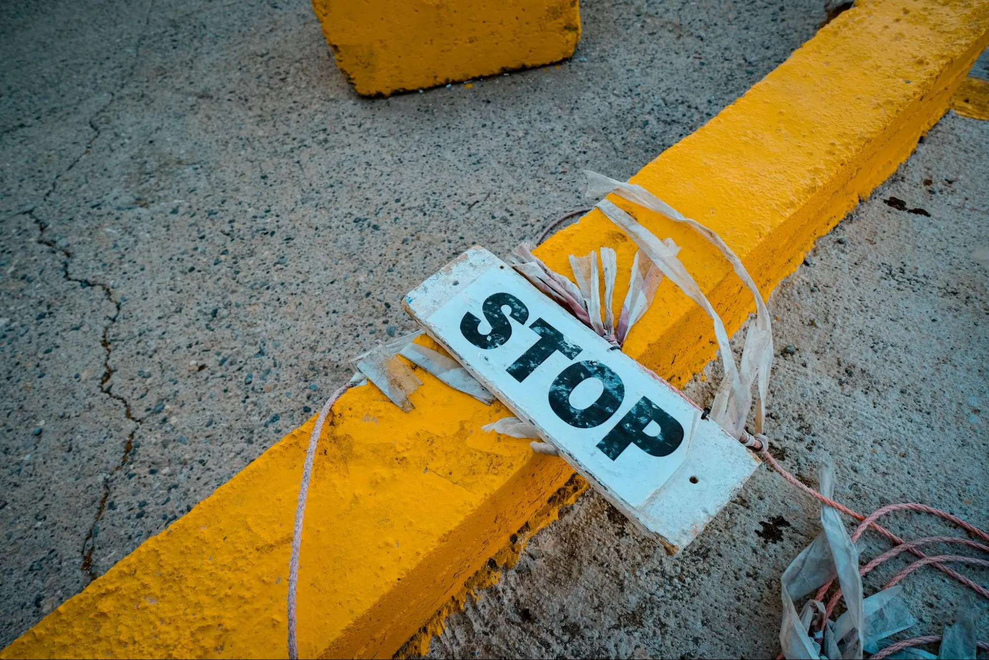A weathered STOP sign tied to a yellow concrete barrier laid across a road, representing a consignment held at the border
