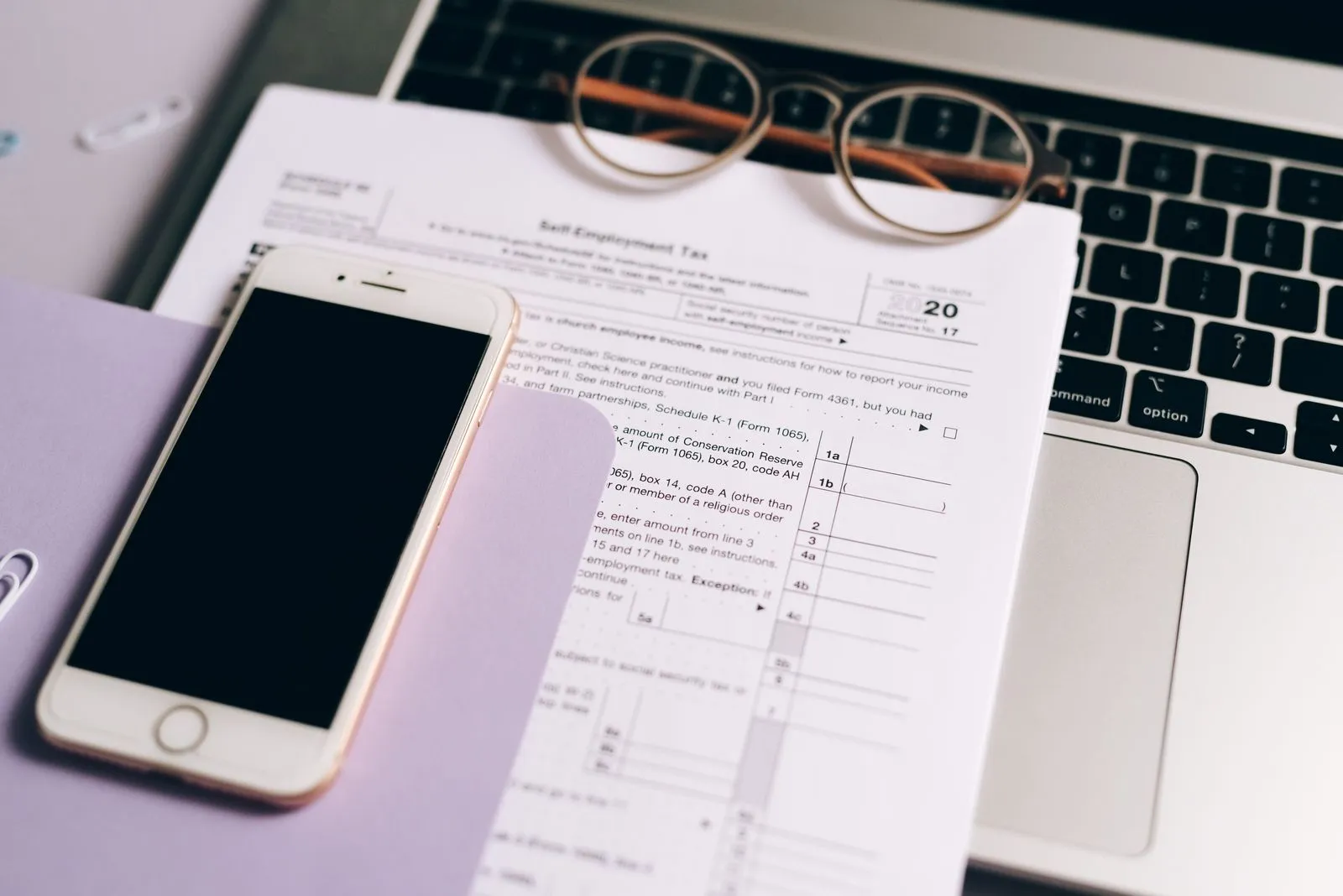 A printed US tax form on a laptop keyboard, with a pair of glasses and a smartphone resting on it
