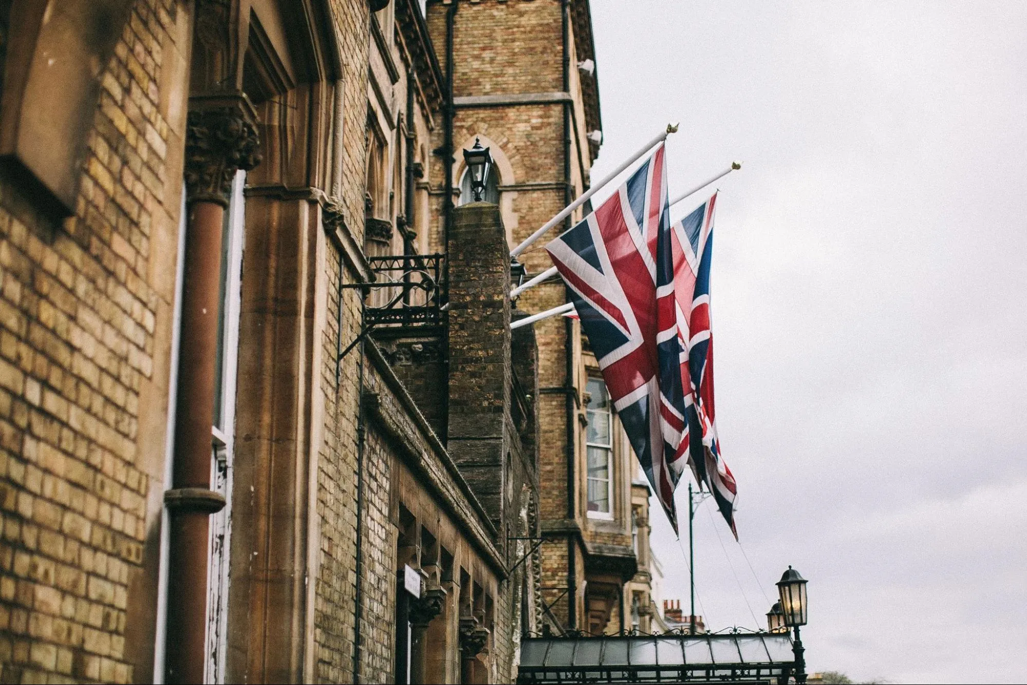 Two Union Jack flags on poles projecting from the brick facade of a Victorian building